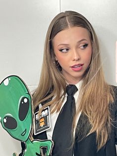 a woman in a suit and tie holding an alien pin