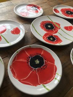 several plates with red flowers painted on them sitting on a wooden table next to each other