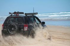 a black jeep driving down a sandy beach next to the ocean