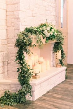 a fireplace with candles and greenery on the mantle