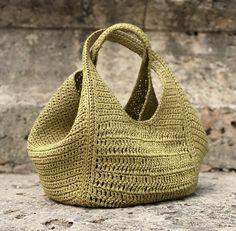 a green crocheted bag sitting on top of a stone floor next to a brick wall