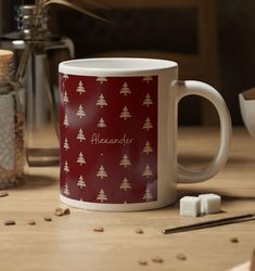 a red and gold christmas mug sitting on top of a wooden table next to spices