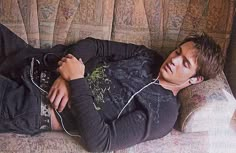 a young man laying on top of a couch with headphones in his ears and listening to music