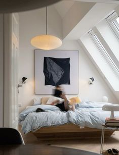 a person sitting on a bed in a room with white walls and slanted ceilings