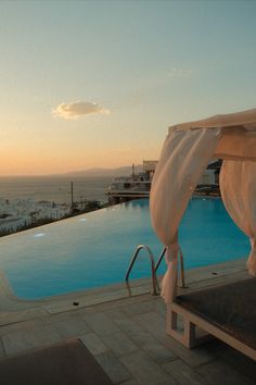 an outdoor swimming pool with white drapes on the roof and sun setting in the background