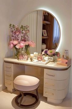 a vanity with flowers and candles on it in front of a round mirror that is lit up