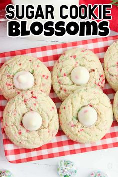 sugar cookie blossoms on a red and white checkered tablecloth with christmas cookies in the background