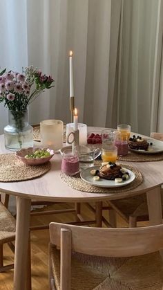 a table set with plates, cups and candles on it in front of a window