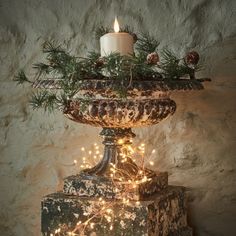 a candle is lit on top of a urn decorated with pine cones and lights