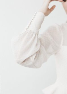 a woman in a white dress holding her hand up to her face