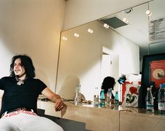 a man sitting in front of a bathroom mirror next to a counter with bottles on it