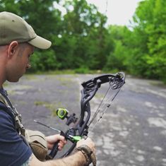 a man holding a bow while standing next to a bike on a road with trees in the background