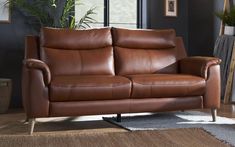 a brown leather couch sitting on top of a wooden floor next to a plant in a living room