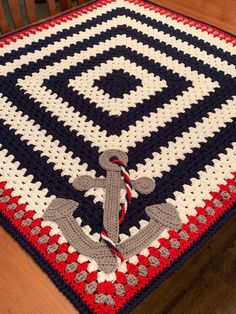 a crocheted blanket with an anchor on it sitting on top of a wooden table