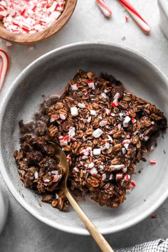 a white bowl filled with chocolate and peppermint granola next to candy canes