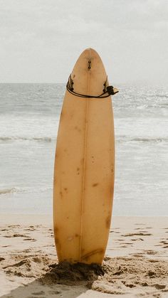 a surfboard sticking out of the sand at the beach with waves in the background