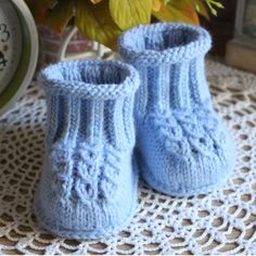 a pair of blue knitted baby booties sitting on top of a doily