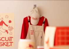 an apron hanging on a wall next to a sign that says biscuit basket and a cup