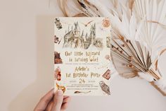 a hand holding up a harry potter birthday card with feathers around it and the hogwart's castle on top