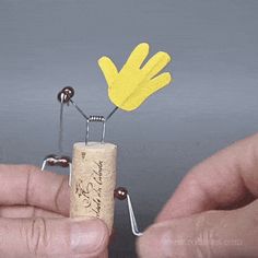 two hands holding a tiny cork with a yellow flower on it and some metal pins sticking out of the cork