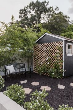 an outdoor garden with black gravel and white flowers on the ground next to a shed