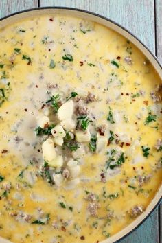 a pot filled with cheese and meat on top of a blue wooden table next to a spoon