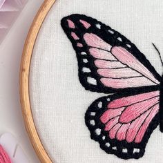 a pink and black butterfly sitting on top of a piece of white fabric next to thread