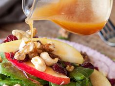 someone pouring dressing onto a salad with apples, walnuts and cranberries