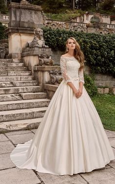 a woman standing in front of some steps wearing a wedding dress with long sleeves and an open back