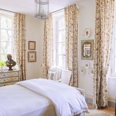 a bedroom with white bedding and floral drapes on the window sill, along with an antique chest of drawers