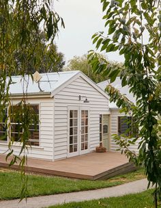 a small white house sitting on top of a wooden deck next to a lush green field