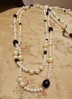 A lovely, long necklace with 2 strands of mainly white and some black and golden beads. Elegant White Multi-strand Long Necklace, Elegant Double Strand Beaded Necklace With Black Beads, Elegant White Double Strand Long Necklace, White Double Strand Pearl Necklace For Party, White Double Strand Pearl Layered Necklace, Elegant White Beaded Chain Layered Necklace, Elegant White Long Necklace With Round Beads, White Beaded Chain Long Necklace, White Long Beaded Necklaces For Party