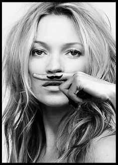 black and white photograph of a woman with fake mustaches on her nose, looking at the camera