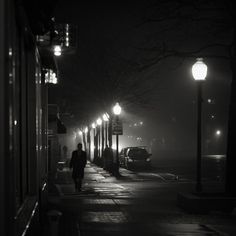 a person walking down a street at night in the fog with lights shining on them