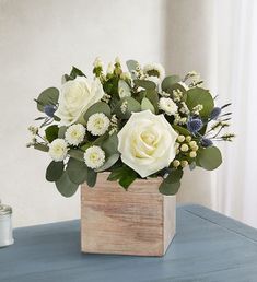 a bouquet of white flowers in a wooden box on a table next to a candle