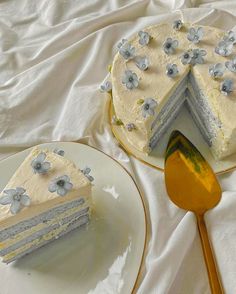 a white cake with blue flowers on it sitting next to a slice of cake and a gold spoon