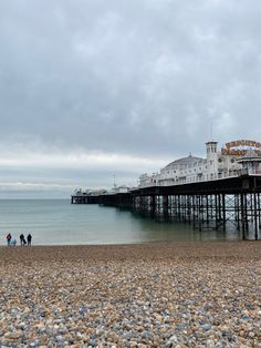 people are walking on the beach next to a large wooden pier in the distance, under a cloudy sky