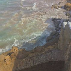 the water is crashing over the stone wall by the ocean's edge, and it looks like waves are coming in from the rocks