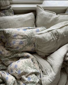 an unmade bed with striped sheets and blue flowers on it, in front of a window