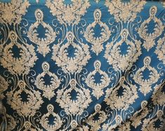 a blue and gold brocaded fabric with white flowers on the bottom half of it