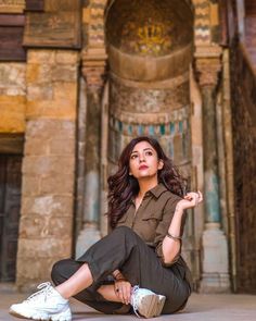 a woman is sitting on the ground in front of an old building and posing for a photo