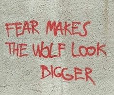 the words fear makes the wolf look bigger written in red on a white wall with graffiti