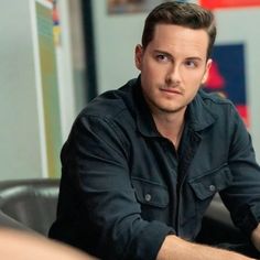 a man sitting at a table with his hand on the desk and looking off into the distance