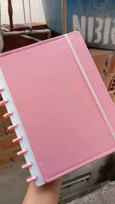 a hand holding a pink and white notebook