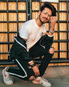 a man sitting on the ground in front of a metal fence with his hand up to his face