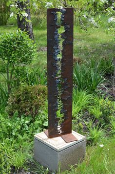 a tall metal sculpture sitting in the middle of a field next to some grass and trees