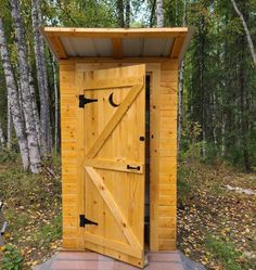 a wooden outhouse in the woods with an open door on it's side