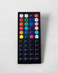 a remote control sitting on top of a white table next to a black box with colored buttons