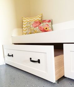 a white bed with drawers underneath it and a pillow sitting on top of the bottom