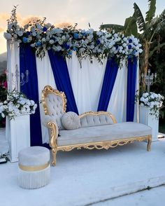 a white couch with blue drapes and flowers on the back is set up for an outdoor ceremony